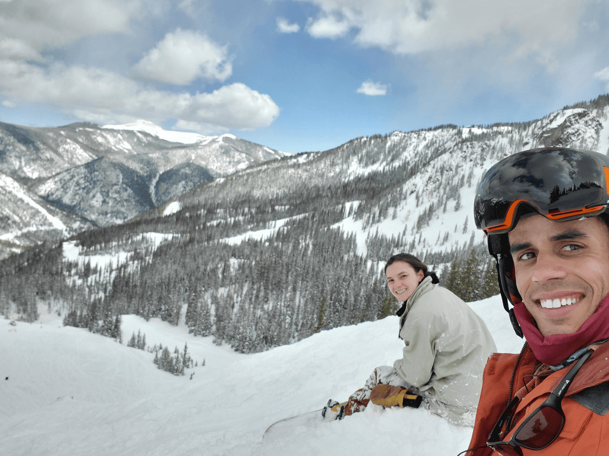 Devin his wife Hannah in their snowboard gear sitting on a snowy mountain